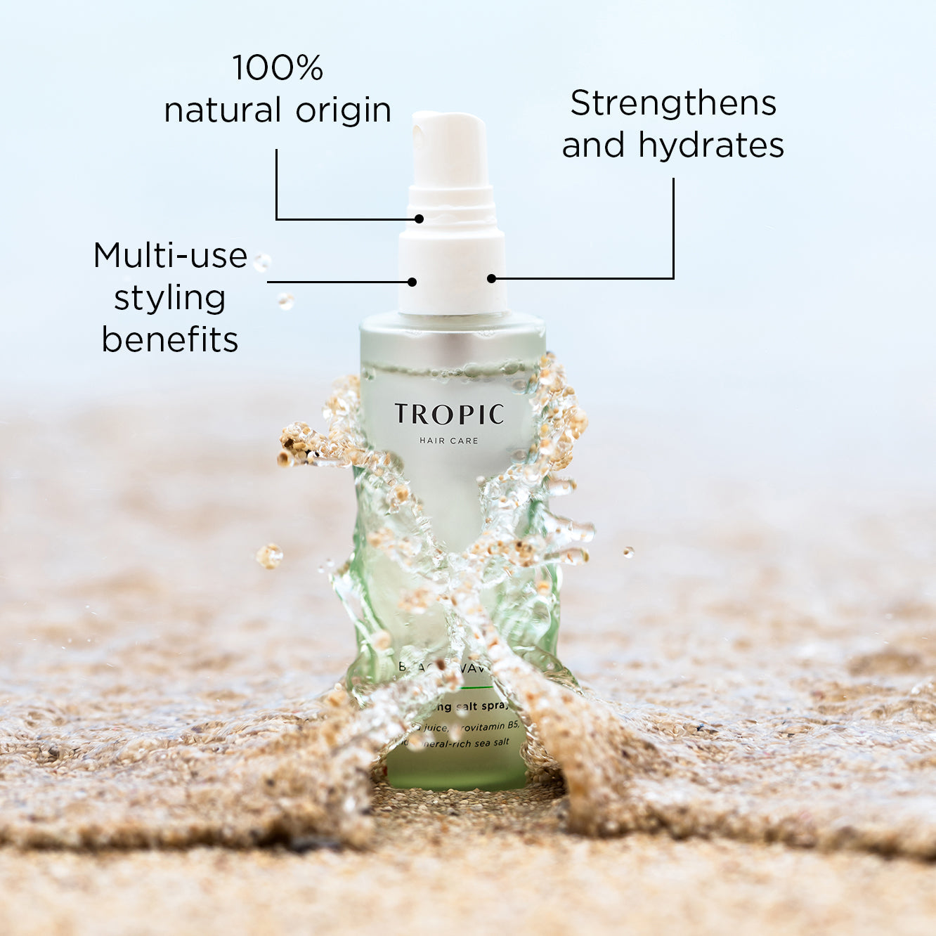 A bottle of Tropic Beach Waves Texturising Salt Spray surrounded by splashing water on a sandy beach. The text highlights key benefits of the product: 100% natural origin, strengthens and hydrates, and multi-use styling benefits.